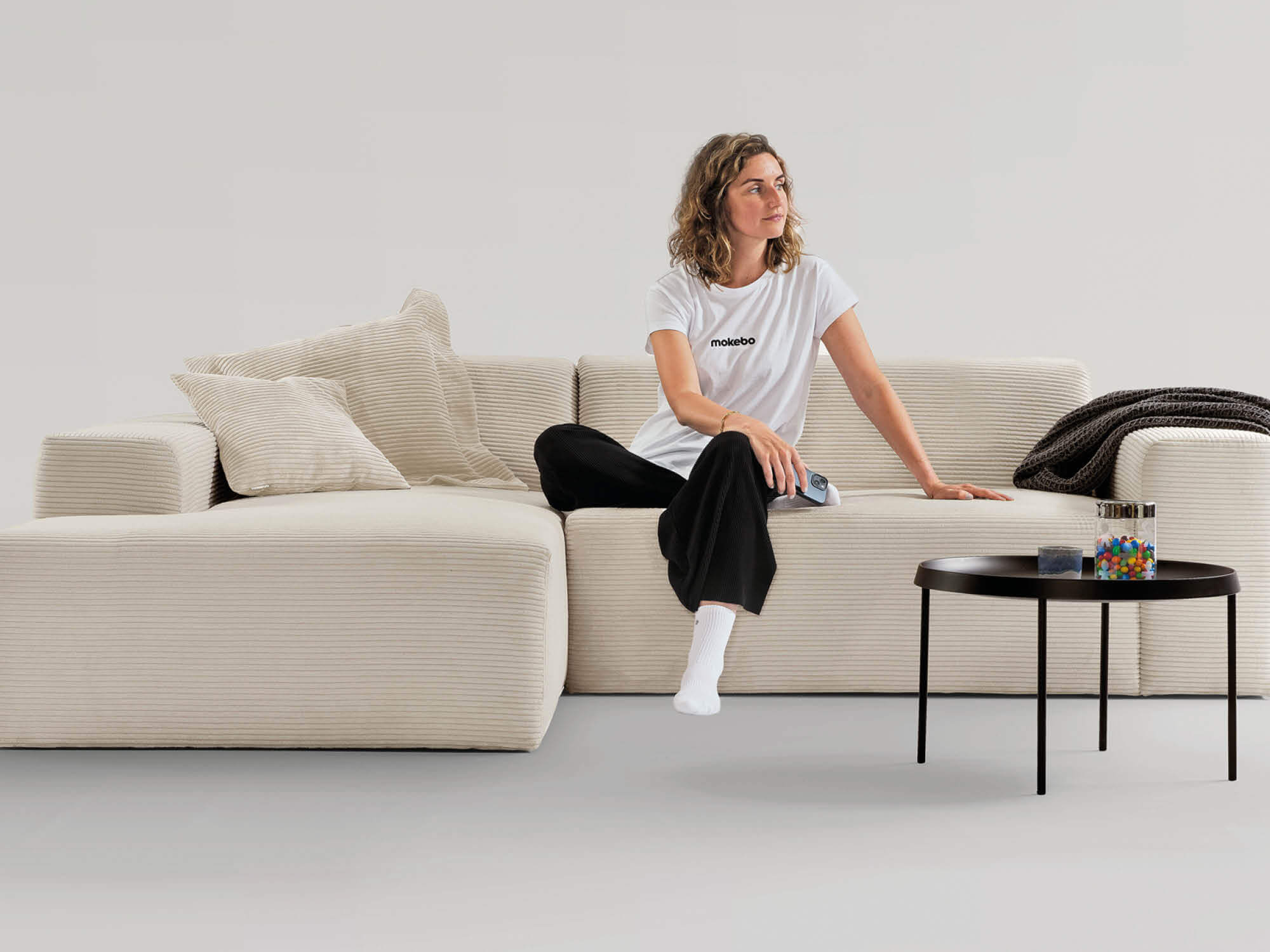 Cordsofa Ecksofa in Beige. Frau sitzt mittig auf dem Sofa und schaut nach links