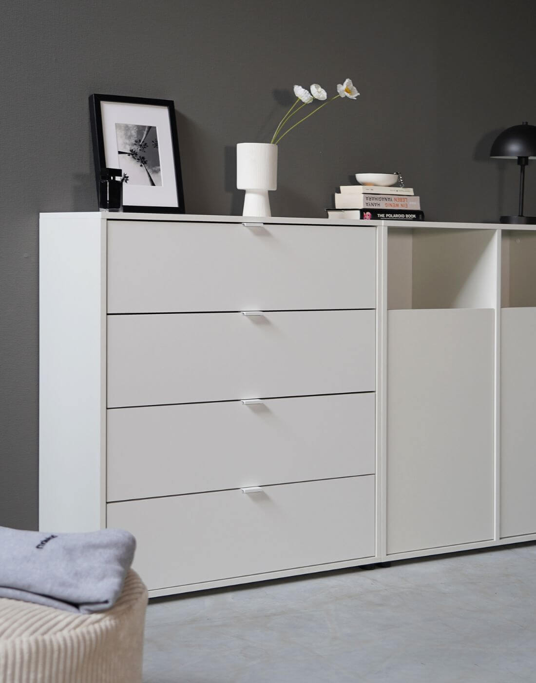 weiße Kommode 'Die Stilvolle' mit vier Fächern neben weißen Wäscheschrank 'Der Wäschehüter' an grauer Wand