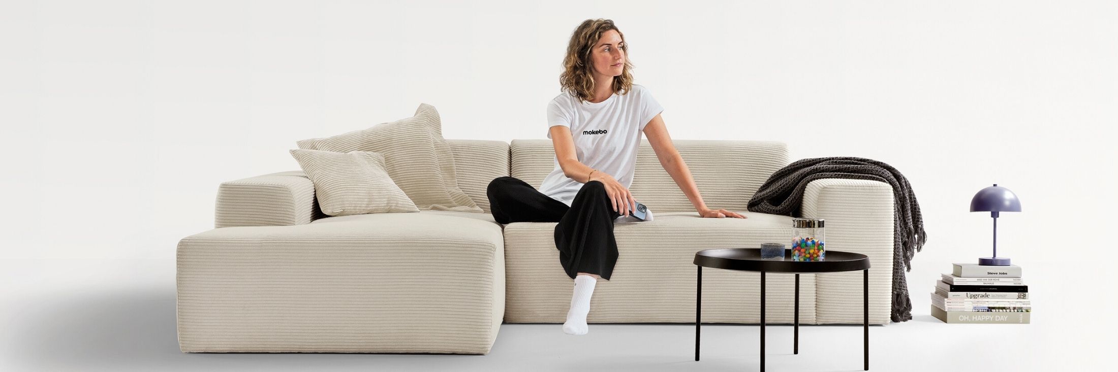 Cordsofa Ecksofa in beige, Frau sitzt mittig auf dem Cordsofa und schaut nach rechts