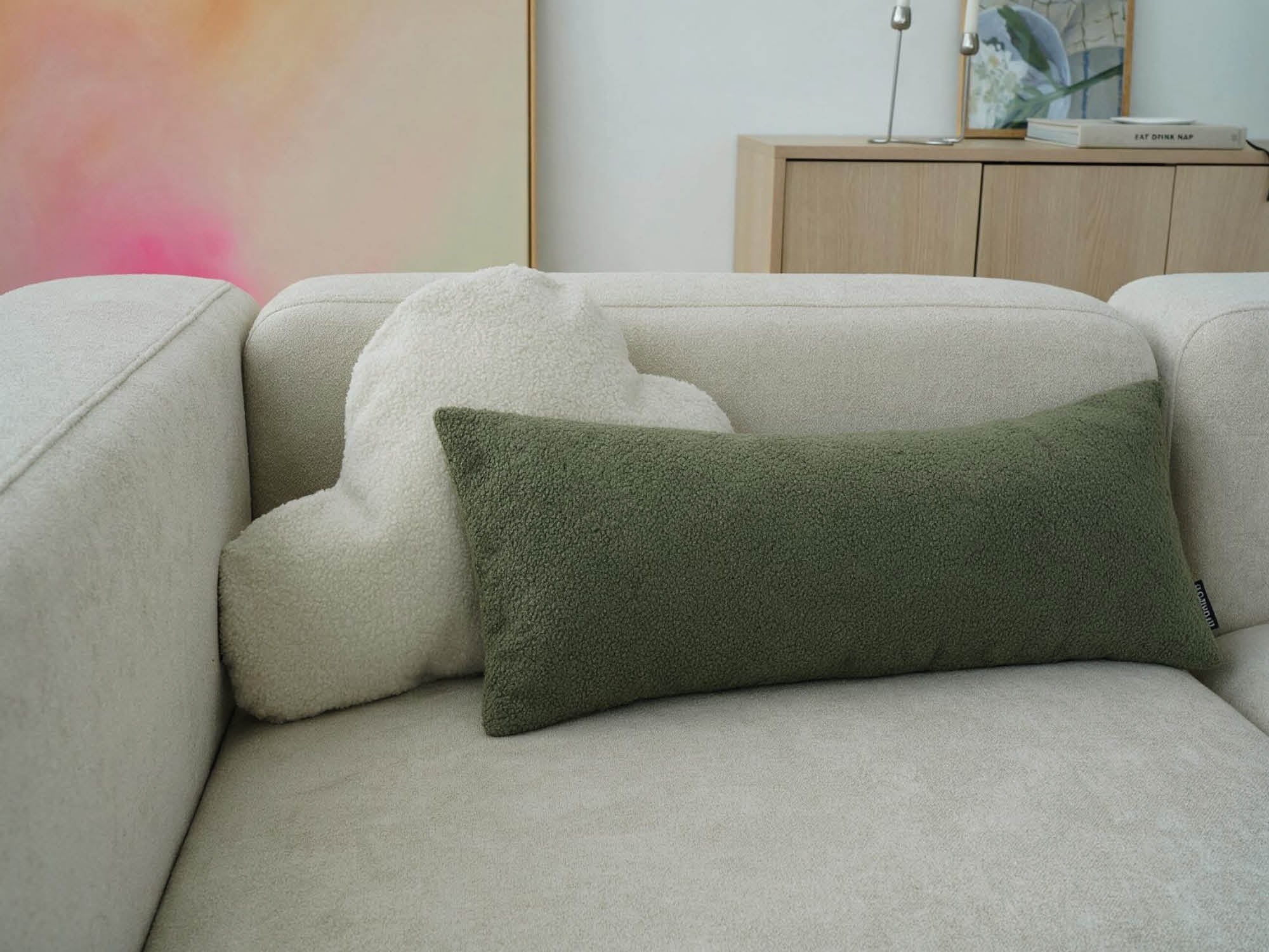 Dekokissen 'Cloud' in hellbeige und Lendenkissen 'Line' in grün auf einem Sofa aneinander 