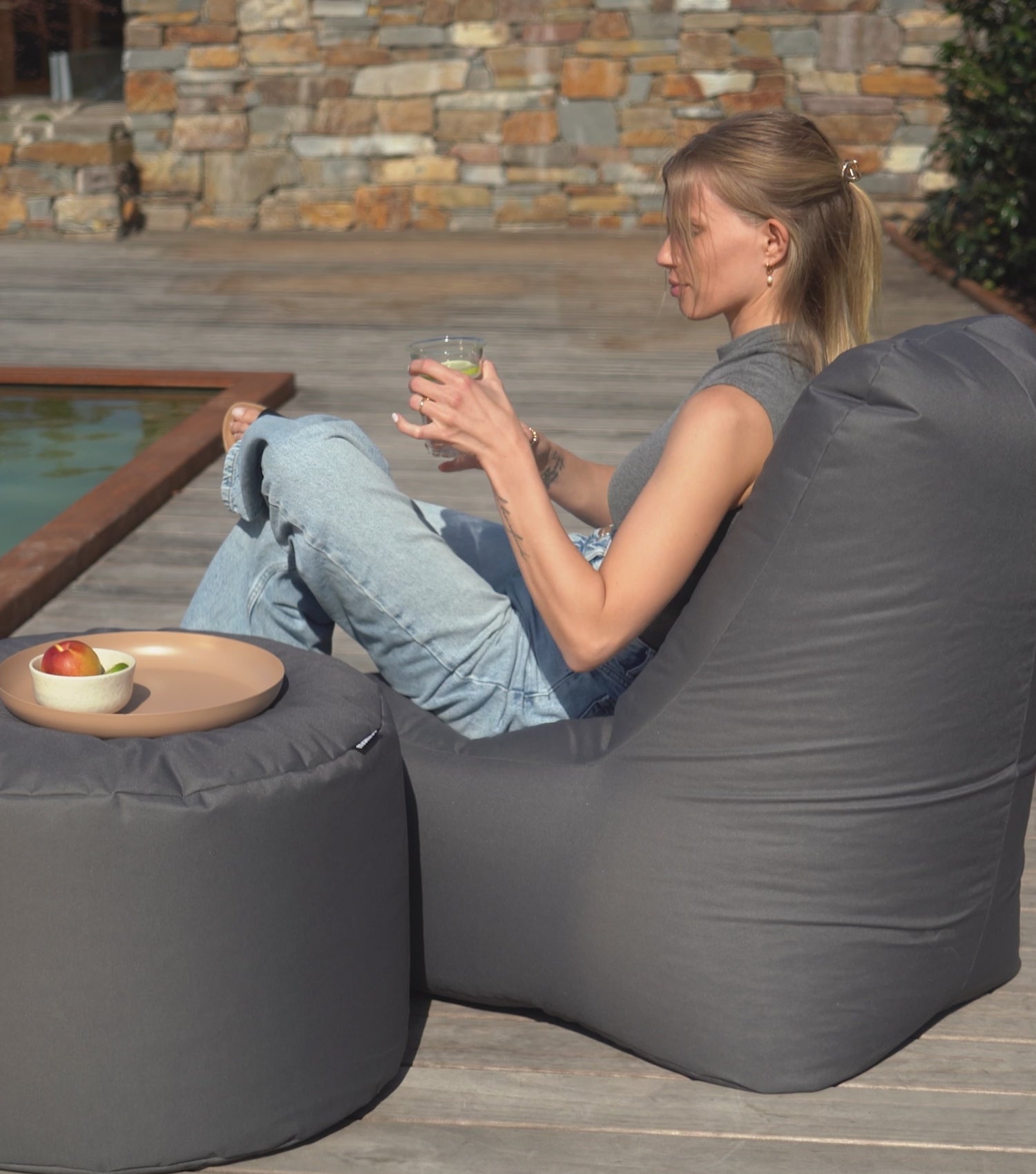 Produktvideo Outdoor Sitzsack Sitzsessel 'Der Däumchendreher' in anthrazit. Sitzsack im Garten. Frau sitzt auf dem Sitzsack und trinkt ein Glas Wasser, Frau arbeitet am Laptop auf dem Sitzsack. 